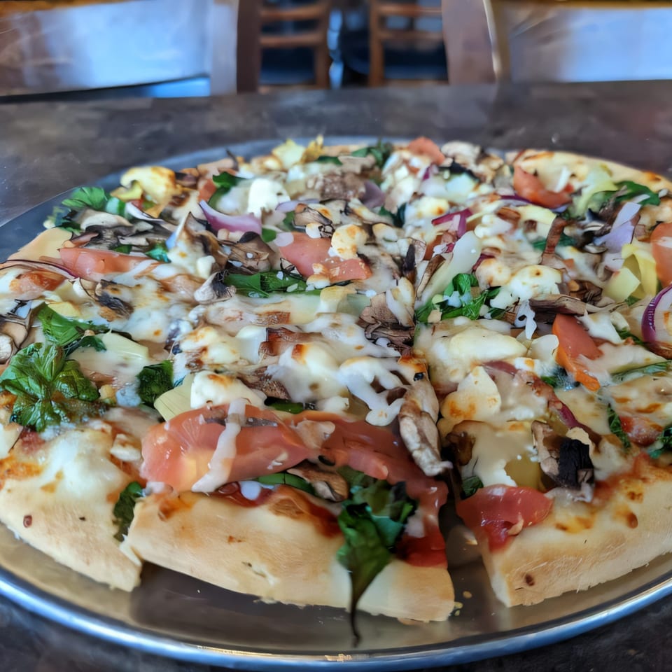 A freshly baked Palio's Pizza with mushrooms, tomatoes, red onion, and spinach on a metal tray.