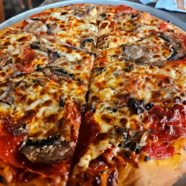 Close-up of a Palio's Pizza Cafe Grapevine pizza with mushrooms and pepperoni, sliced and ready to eat.