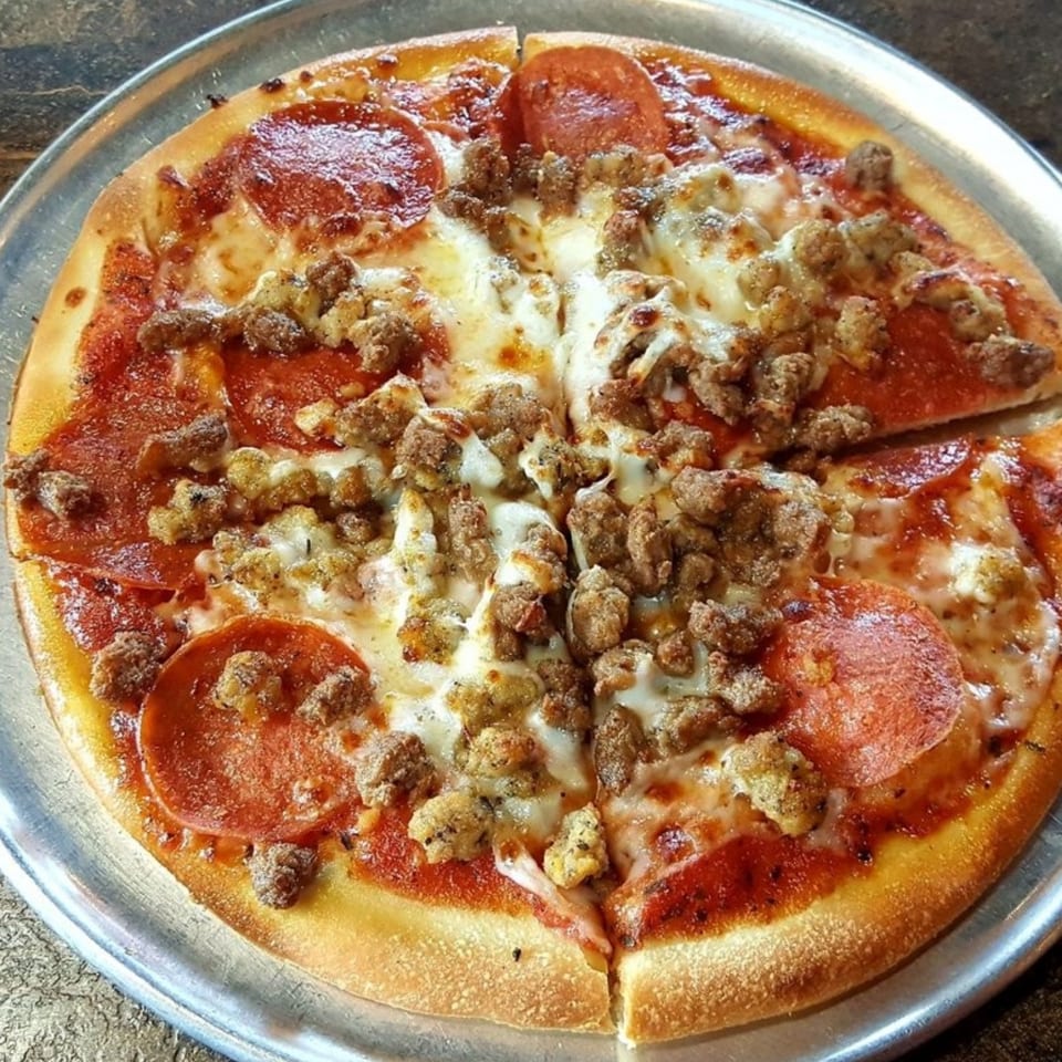 A Palio's Pizza Cafe Grapevine pizza with pepperoni and sausage on a metal tray.